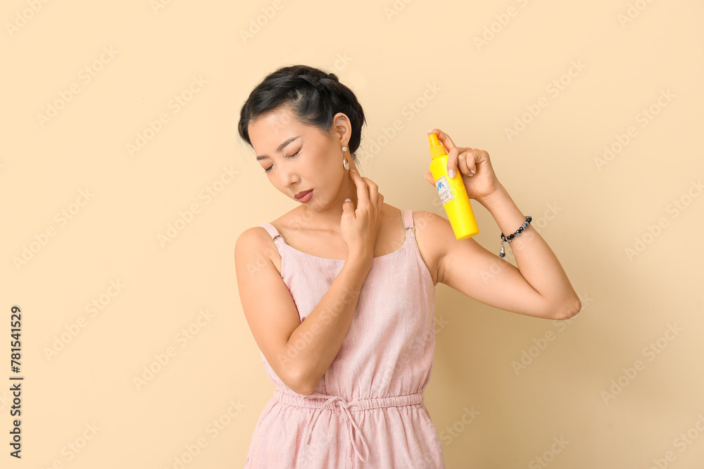 Young Asian woman with mosquito repellent on beige background