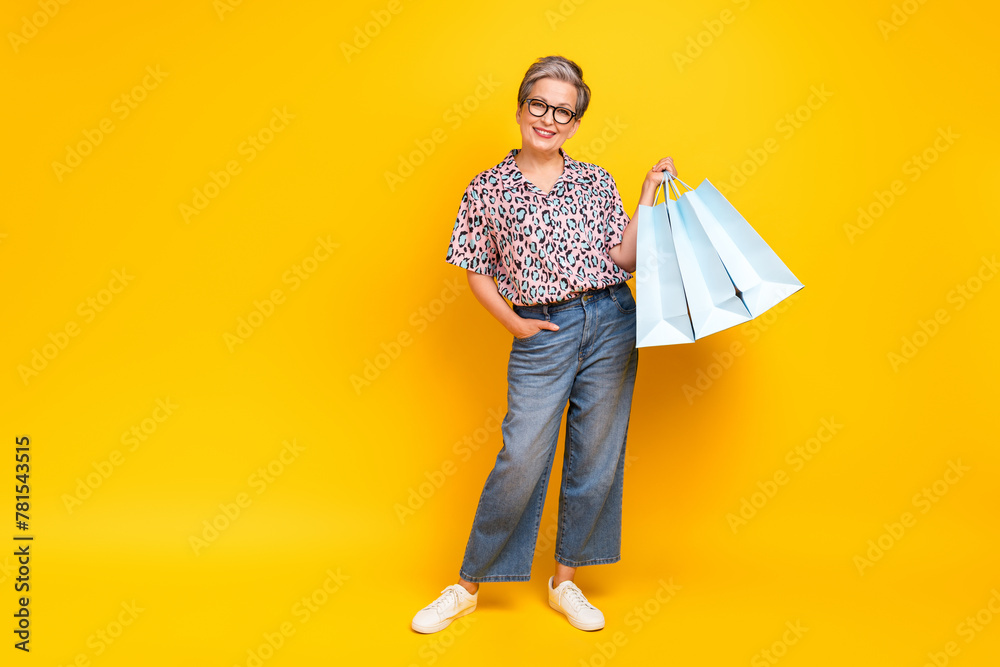 Full length photo of lovely senior lady hold shopping bags dressed stylish leopard print garment isolated on yellow color background - obrazy, fototapety, plakaty 