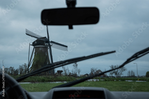 A typically miserable rainy day in the Netherlands view from inside a car. windmill and grey stormy clouds with rear view mirror, dashboard and windscreen wipers on Dutch bad weather day in Holland