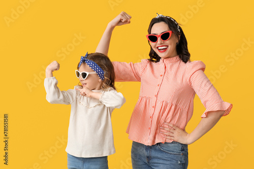 Beautiful pin-up woman and her daughter in sunglasses showing muscles on yellow background