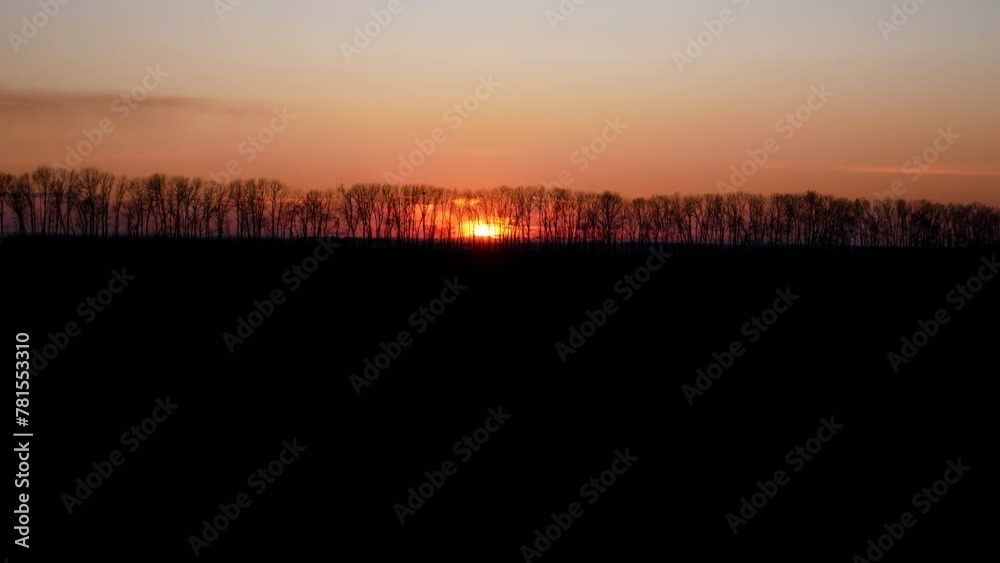 Sunset. The red sun sets behind the trees. In the foreground is a field of black earth in shadow. Sunset. The red sun sets behind the trees. In the foreground is a field of black earth in shadow.
