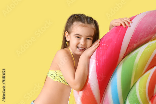 Cute little girl with inflatable mattress in shape of lollipop on yellow background © Pixel-Shot