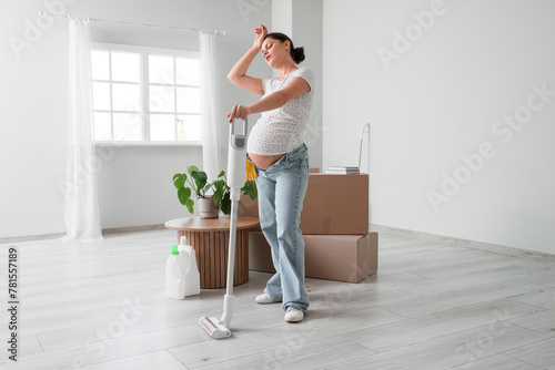 Tired pregnant woman with vacuum cleaning in new apartment