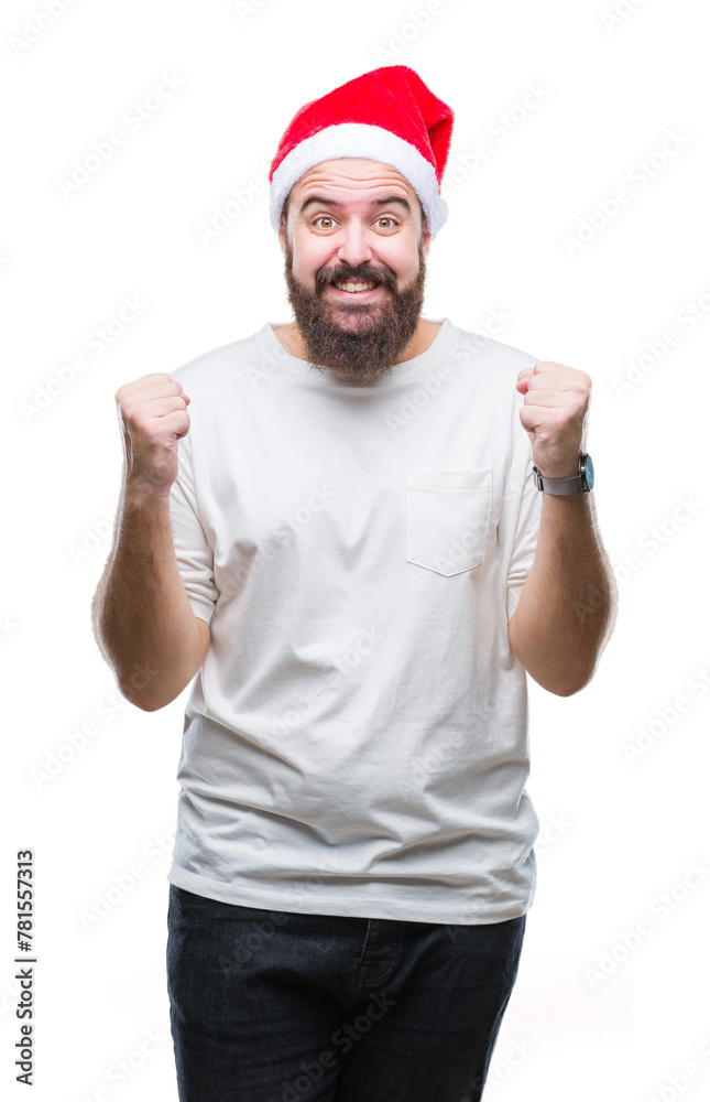Young caucasian hipster man wearing christmas hat over isolated background celebrating surprised and amazed for success with arms raised and open eyes. Winner concept. Young caucasian hipster man wearing christmas hat over isolated background celebrating surprised and amazed for success with arms raised and open eyes. Winner concept.