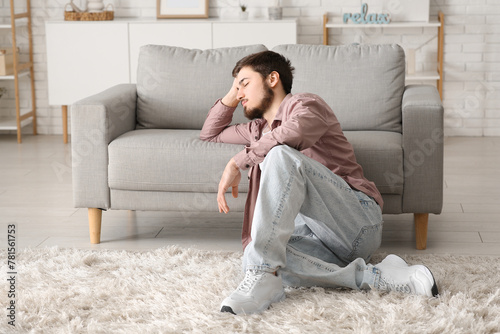 Tired young man sitting near sofa at home