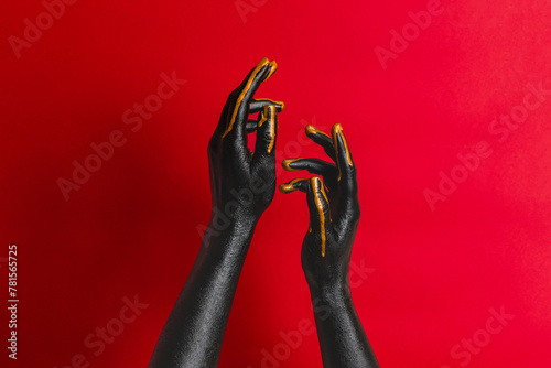 Black and gold colors painted woman's hands on her skin with red background. High Fashion art concept