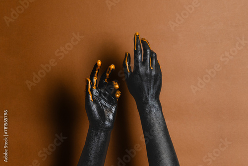 Elegant woman's hands with black and gold painted on her skin on brown background. High Fashion art concept