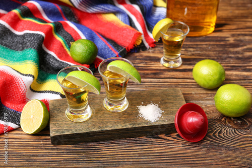 Shots of tequila with slices of lime and salt on wooden background