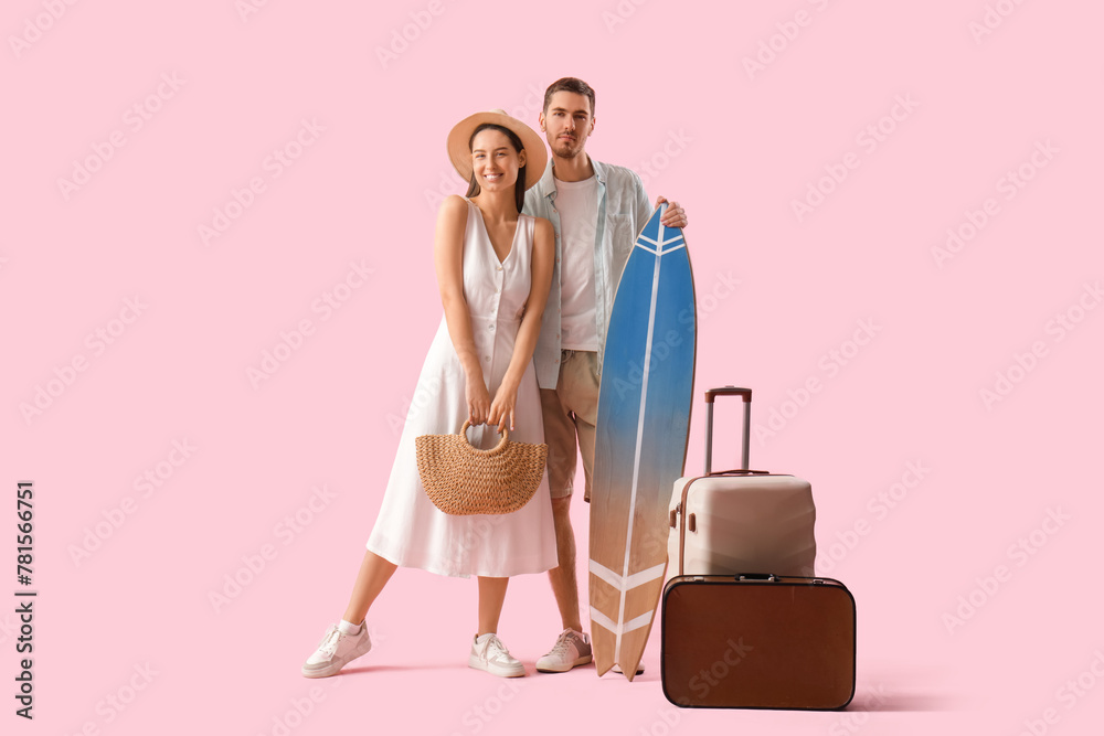 Beautiful young happy couple of tourists with suitcases and surfboard on pink background