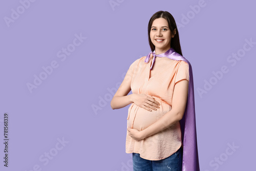 Beautiful young pregnant woman in superhero cape on lilac background