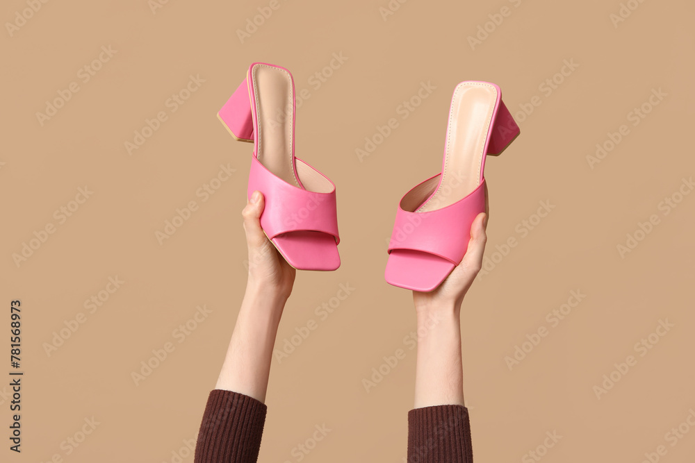 Female hands with stylish pink sandals on brown background