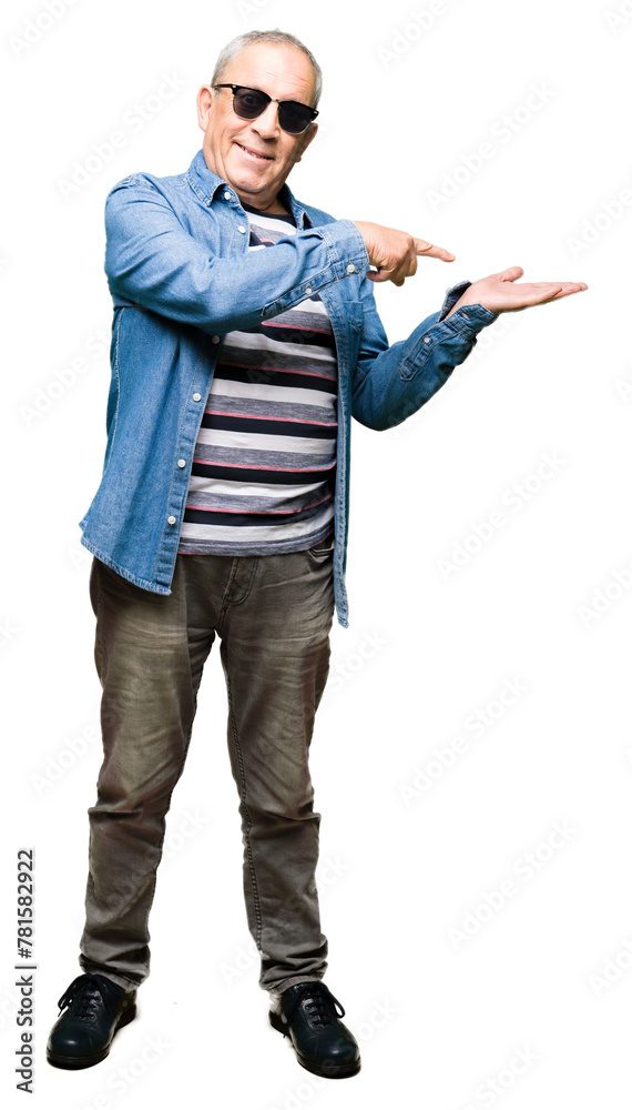 Handsome senior man wearing denim jacket and sunglasses amazed and smiling to the camera while presenting with hand and pointing with finger. Handsome senior man wearing denim jacket and sunglasses amazed and smiling to the camera while presenting with hand and pointing with finger.