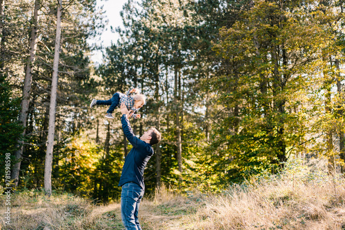 Dad throws up a laughing little girl on a sunny lawn in the forest