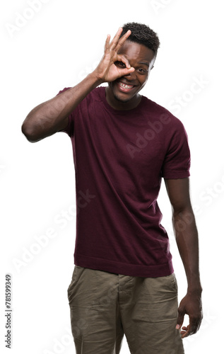 Young african american man with happy face smiling doing ok sign with hand on eye looking through fingers