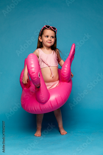 Happy child girl in pink swimsuit with swimming ring flamingo on a colored blue background. Travel, summer beach concept.