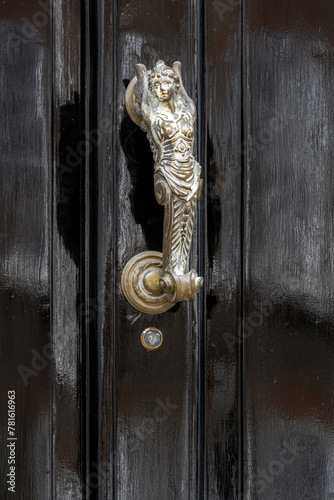 Metal door knocker on a black wooden door in the shape of a mermaid