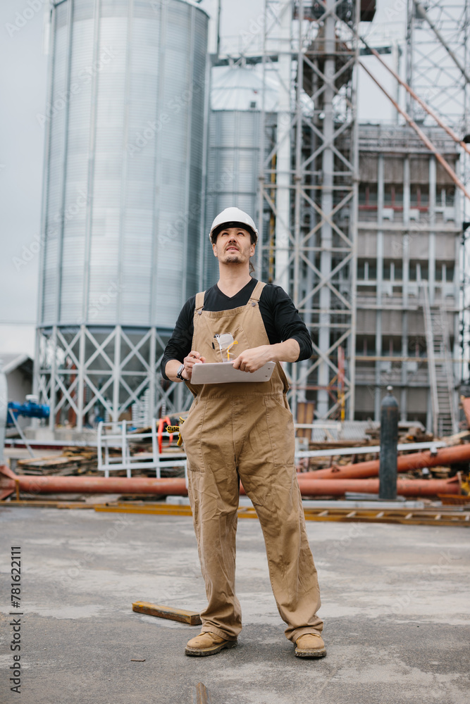 Engineer, industrial worker in front of silos full of grain.