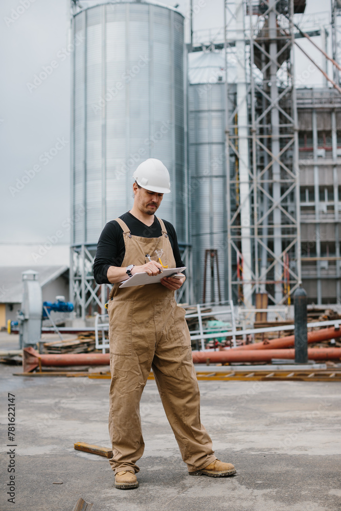 An engineer works in an industrial area on the background of a silo with grain. An engineer works in an industrial area on the background of a silo with grain.