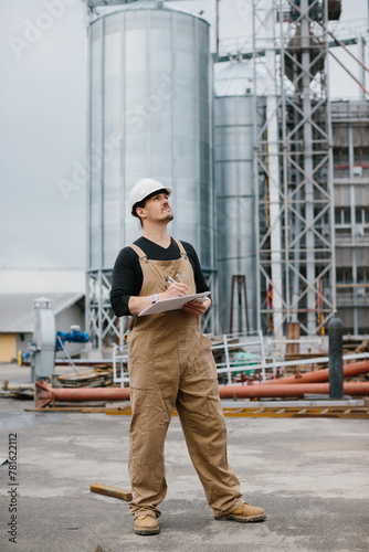 Engineer, industrial worker in front of silos full of grain.