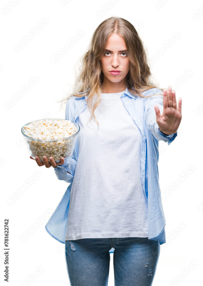 Beautiful young blonde woman eating popcorn over isolated background with open hand doing stop sign with serious and confident expression, defense gesture Beautiful young blonde woman eating popcorn over isolated background with open hand doing stop sign with serious and confident expression, defense gesture