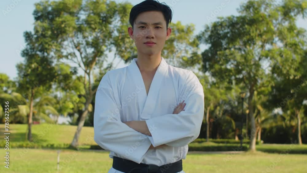 Medium portrait of gen Z Asian sportsman wearing dobok and black belt looking at camera in city park Medium portrait of gen Z Asian sportsman wearing dobok and black belt looking at camera in city park
