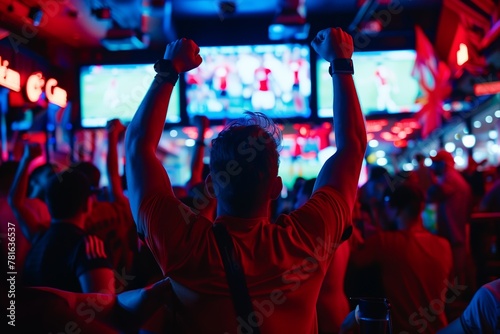 A silhouette of an elated sports fan is captured against the vibrant backdrop of a bar's televised sports event. 