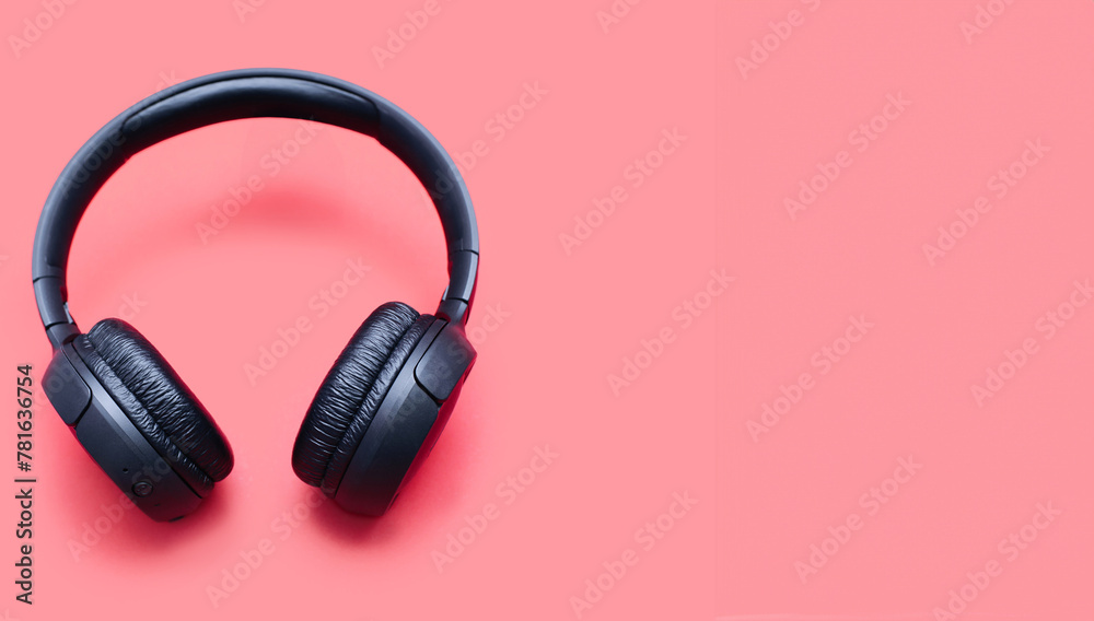 Wireless headphones in black color isolated on red background with space for text. On-ear wireless headphones for playing games and listening to music tracks close-up. Wireless Bluetooth headphones Wireless headphones in black color isolated on red background with space for text. On-ear wireless headphones for playing games and listening to music tracks close-up. Wireless Bluetooth headphones