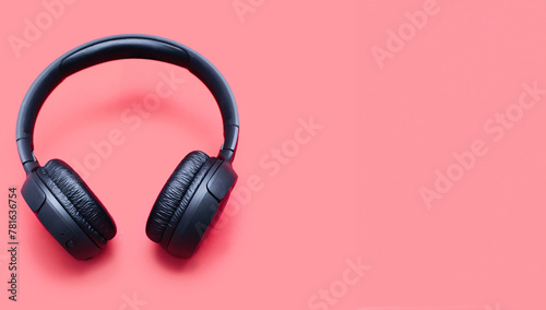 Wireless headphones in black color isolated on red background with space for text. On-ear wireless headphones for playing games and listening to music tracks close-up. Wireless Bluetooth headphones