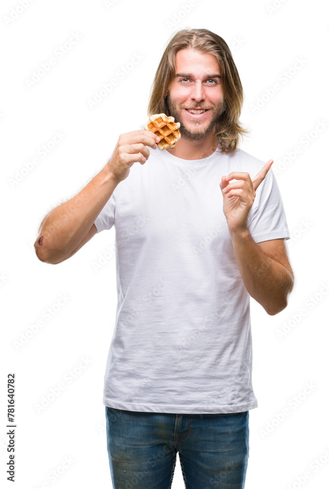 Young handsome man with long hair over isolated background eating waffle very happy pointing with hand and finger to the side Young handsome man with long hair over isolated background eating waffle very happy pointing with hand and finger to the side