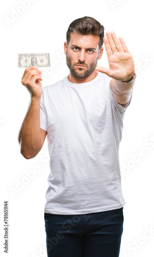 Young handsome man holding dollars over isolated background with open hand doing stop sign with serious and confident expression, defense gesture