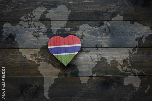 wooden heart with national flag of gambia near world map on the wooden background.