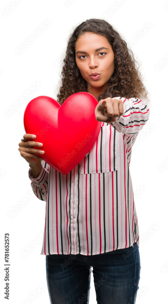 Young hispanic woman in love holding red heart pointing with finger to the camera and to you, hand sign, positive and confident gesture from the front