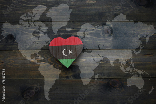 wooden heart with national flag of libya near world map on the wooden background.