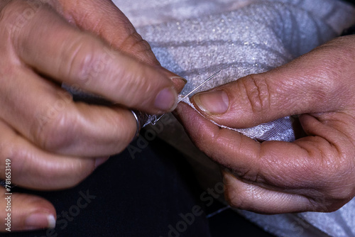 Close-up view of woman's hands in sewing process. Sewing fabric by hand with needle at workplace. Dressmaker's hands holding fabric for making tablecloths. Handmade, hobby, small business concept