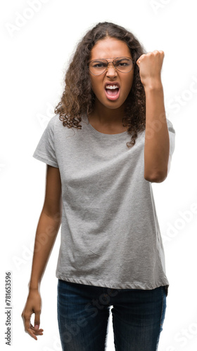 Beautiful young hispanic woman wearing glasses angry and mad raising fist frustrated and furious while shouting with anger. Rage and aggressive concept.