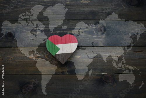 wooden heart with national flag of sudan near world map on the wooden background. photo
