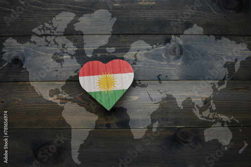 wooden heart with national flag of kurdistan near world map on the wooden background.