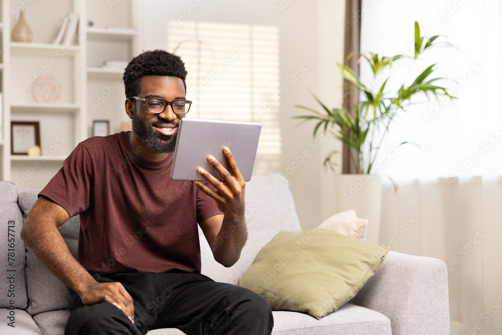 Cheerful Young Man Enjoying Tablet On Cozy Sofa At Home. Positive African American Smiling, Casual, Leisure, Comfort, Technology.