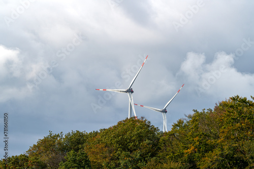Wind turbines behind the trees under the cloudy sky