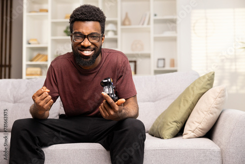 Happy Man With Glasses Holding Game Controller Winning Video Game At Home. Excitement, Entertainment, and Leisure Indoors Concept.