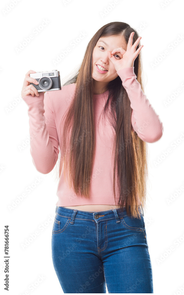 Young Chinese woman over isolated background taking pictures using vintage camera with happy face smiling doing ok sign with hand on eye looking through fingers Young Chinese woman over isolated background taking pictures using vintage camera with happy face smiling doing ok sign with hand on eye looking through fingers