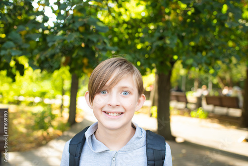 portrait of a smiling, 11 year old schoolboy with a backpack in the park