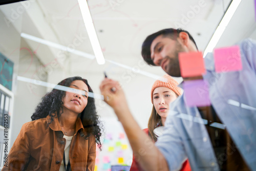 Business professional uses a glass wall covered with sticky notes to outline processes during a team meeting.