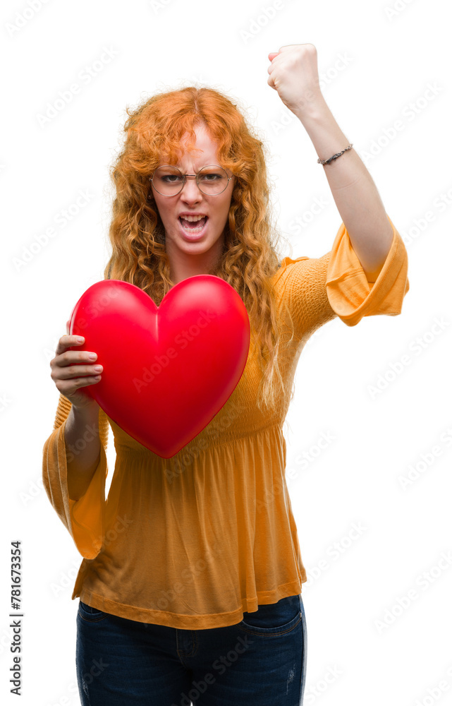 Young redhead woman in love holding red heart annoyed and frustrated shouting with anger, crazy and yelling with raised hand, anger concept Young redhead woman in love holding red heart annoyed and frustrated shouting with anger, crazy and yelling with raised hand, anger concept