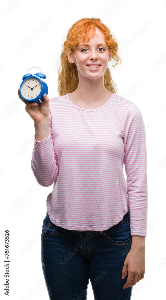 Young redhead woman holding alarm clock with a happy face standing and smiling with a confident smile showing teeth Young redhead woman holding alarm clock with a happy face standing and smiling with a confident smile showing teeth