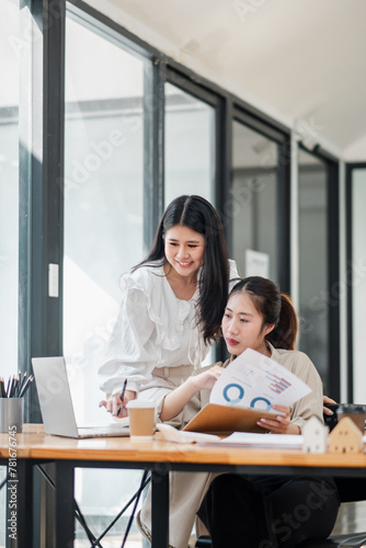 Two professional women engaged in reviewing a business report together in a modern office setting with a laptop on the desk.