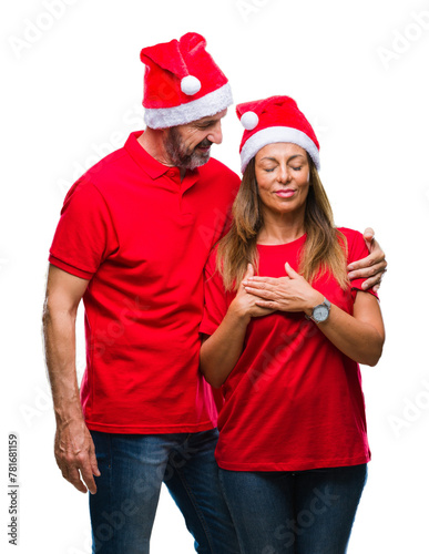 Middle age hispanic couple wearing christmas hat over isolated background smiling with hands on chest with closed eyes and grateful gesture on face. Health concept.