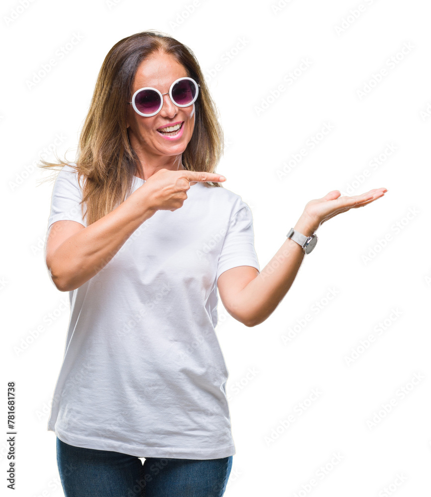 Middle age hispanic woman wearing fashion sunglasses over isolated background amazed and smiling to the camera while presenting with hand and pointing with finger. Middle age hispanic woman wearing fashion sunglasses over isolated background amazed and smiling to the camera while presenting with hand and pointing with finger.