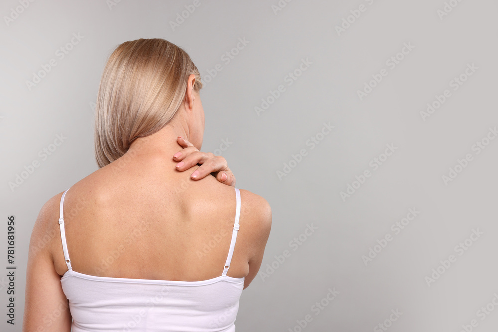 Woman suffering from pain in her neck on grey background, back view. Space for text