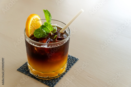 Iced coffee mixed with orange juice, two tones layer decoration with rosemary and piece of orange on wooden background